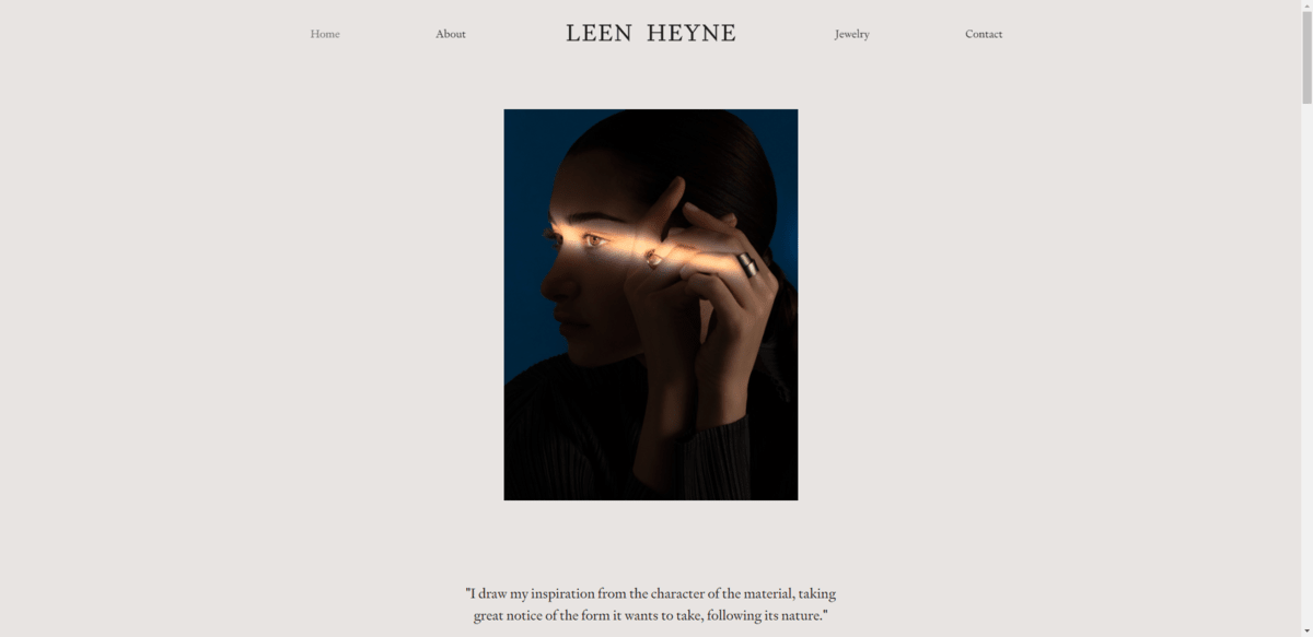 Leen Heyne hyper-minimal design The hero section from the Leen Heyne website. Atop the oversized beige background is a dark photo of a model’s face and hands. There’s a single line of light shining through to reveal one of the jewelry artist’s rings.