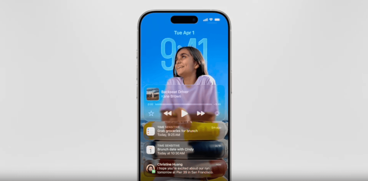 Liquid Glass lock screen In this Liquid Glass iPhone lock screen example, we see a smiling girl in front of the time (which is Liquid Glass). In front of the girl is an audio player that says “Backseat Driver” by Kane Brown along with 3 notifications for a tasks, calendar appointment, and text. These 3 cards and audio player are semi-transparent.